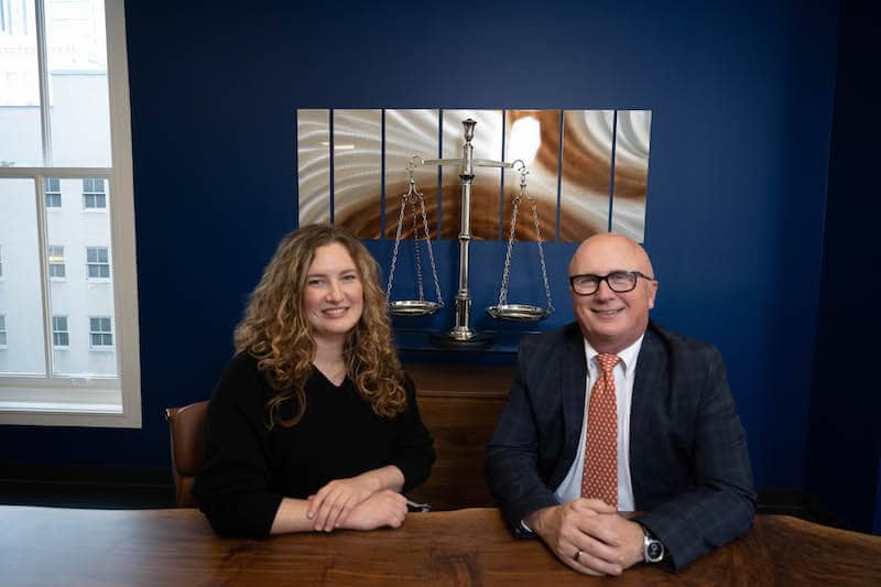 Savannah Lee and personal injury sttorney Jim Dwyer smile at the camera from their Bridge City Law office